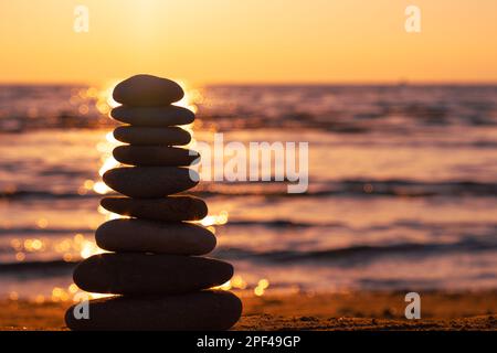 Balanced pebble pyramid silhouette on the beach on sunset with Sea on the background. Zen stones on the sea beach, meditation, spa, harmony, calmness. Stock Photo