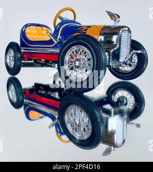 Toy racer car is a mirror image in macro style. Big black tire wheel is center. Play or display vehicle for fun. Colorful yellow, blue, red. & vintage. Stock Photo