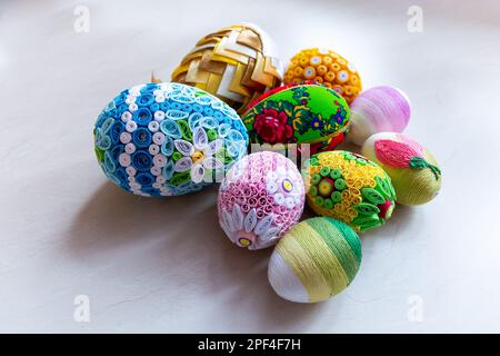 Colorful Easter eggs with floral ornaments, origami decorations and crewel wool against white background, different techniques of Easter eggs decor. Stock Photo
