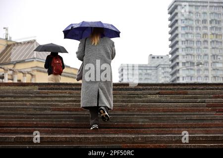 Woman with umbrella walking up the steps on city buildings background. Rain in spring city Stock Photo
