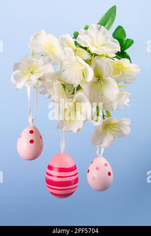 Beautiful arrangement of pink Easter eggs hanging from a flowery branch against a calm blue backdrop Stock Photo