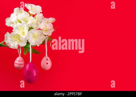Colorful springtime banner featuring three pink Easter eggs delicately suspended from a blooming branch, set against a vibrant red background Stock Photo