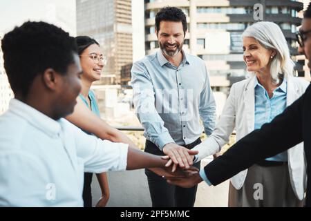 We keep each other motivated. a diverse group of businesspeople standing outside together and stacking her hands. Stock Photo