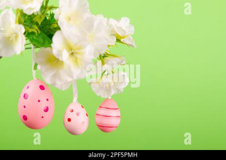 Capture the essence of Easter with this picturesque image of three pink eggs hanging from a delicate branch in full bloom, contrasting against light g Stock Photo