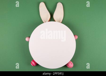 Easter eggs, white circles, and bunny ears decorate a green background Stock Photo