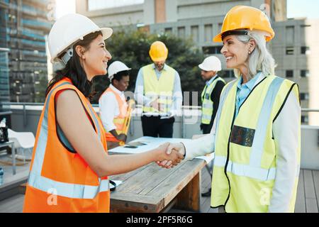 Lets get to work. two contractors standing outside together and shaking hands while their colleagues work behind them. Stock Photo