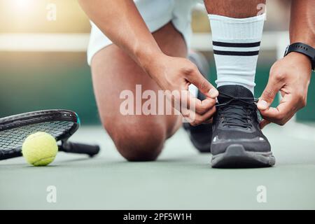 Closeup of unknown indian tennis player getting ready and tying shoelaces on court. Ethnic fit athlete kneeling alone before playing match. Sporty man Stock Photo