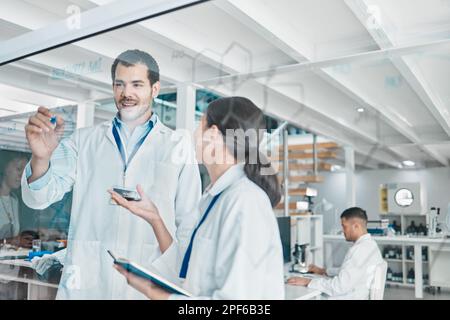 Working on a new and wonderful idea. two young scientists brainstorming with notes on a glass screen in a lab. Stock Photo