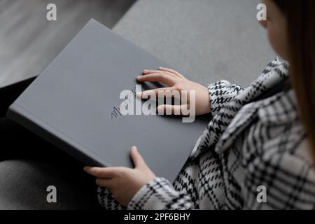 The girl is sitting, holding a gray leather photo book with an imprint of a memory in her hands Stock Photo