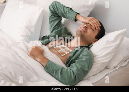 Ill young man with mustard plaster on his chest lying in bedroom Stock Photo