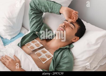 Ill young man with mustard plasters on his chest lying in bedroom Stock Photo