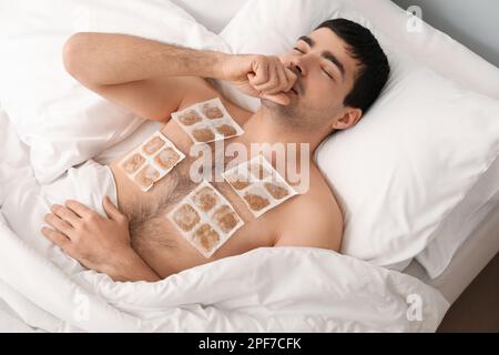 Ill young man with mustard plasters on his chest lying in bedroom Stock Photo