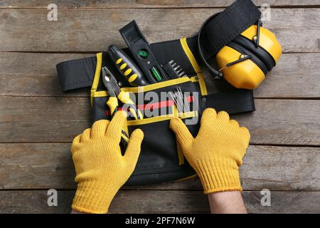 Male hands in gloves taking tools from belt on wooden table Stock Photo