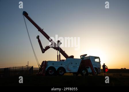 DAF eight-wheeled wrecking truck silhoueted by the low sun on a Summer evening above the M6 in Cumbria Stock Photo