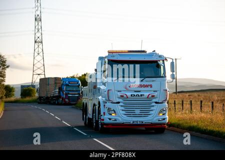 DAF eight-wheeled wrecking truck driving on an A road with another truck and moorland in the background near to dusk Stock Photo