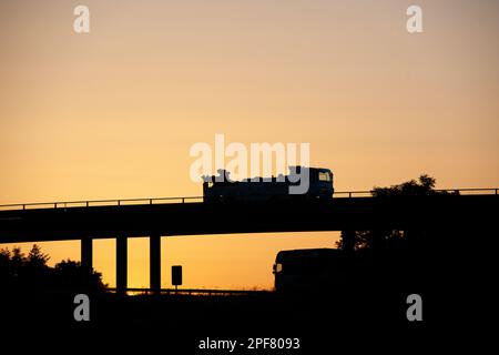 DAF eight-wheeled wrecking truck driving across a bridge over the M6 motorway in Cumbria ar night, with another truck passing underneath Stock Photo