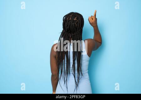 Young african american woman wearing casual dress standing over isolated blue background Posing backwards pointing ahead with finger hand Stock Photo