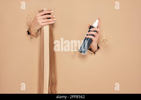 Hands with flowers hold strands of hair for extensions on a beige background. Stock Photo