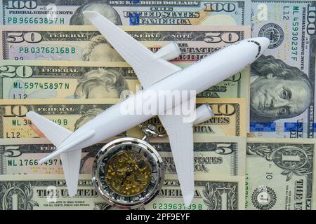 Passenger plane and pocket watch sitting on US currency bills of different denominations showing concept high cost of flying, time  Stock Photo