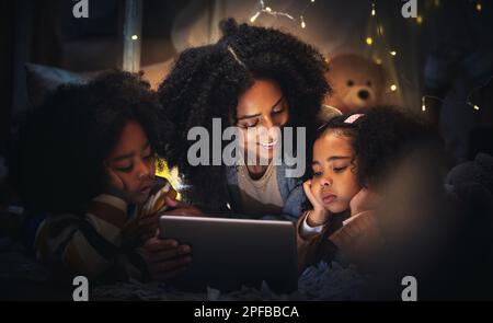 Tablet, night a mother reading to her children in a tent while camping in the bedroom of their home together. Black family, story or kids with a woman Stock Photo