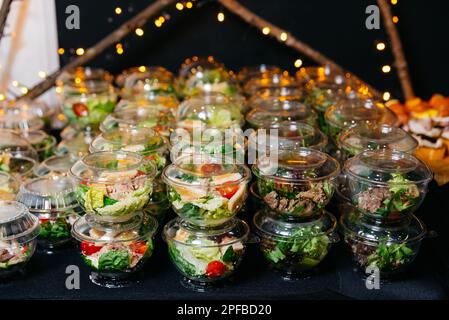 Many portions of various salads with meat and vegetables in plastic serving dishes with lids. Сatering serving portions of salads on the table. Buffet Stock Photo