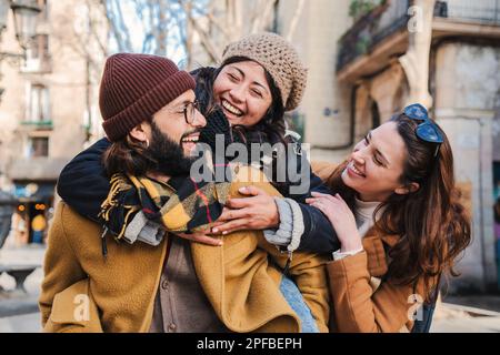 Multiracial group of three happy friends having fun and laughing together. Bearded male giving his girlfriend a piggyback ride. Tourist hugging each other and enjoying a travel trip in Europe. High quality photo Stock Photo