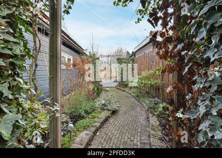 an alley with plants growing on the side and brick walkway leading up to the front door, through which is covered in ivys Stock Photo