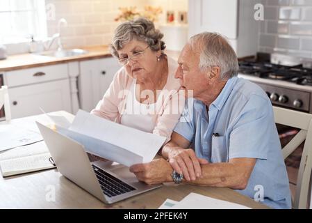 Our most heroic pledge. an elderly couple using a laptop together in the kitchen at home. Stock Photo