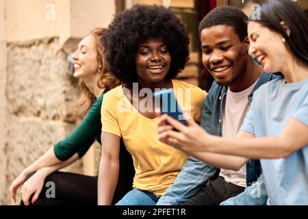 Happy multiethnic group of friends using the mobile outdoors Stock Photo