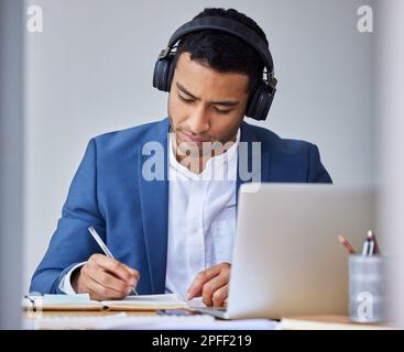 Taking important notes. a young businessman taking notes while using his laptop. Stock Photo