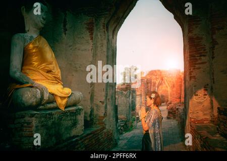 woman wearing thai tradition suit praying to old buddha statue in old temple at ayutthaya one of world heritage site of unesco thailand Stock Photo