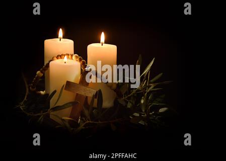 Easter religious background with three burning candles illuminating christian cross and olive branches around in the twilight. Front view. Stock Photo