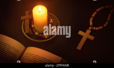 Christian spiritual environment for praying with candle illuminating the symbol of the cross and bible on black table at night. Top elevated view. Stock Photo