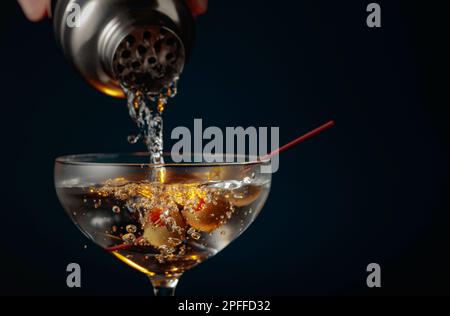 Martini with green olives. The cocktail is poured from a shaker into a glass. Stock Photo