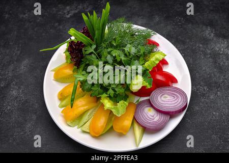 Chopped fresh vegetables, tomatoes, onions, bell peppers, cucumbers and herbs, green onions, dill and parsley on a plate. Close up Stock Photo
