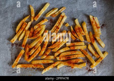 Spicy potato sticks baked in the oven with smoked paprika spice. Home made fries on parchment paper in flat lay Stock Photo