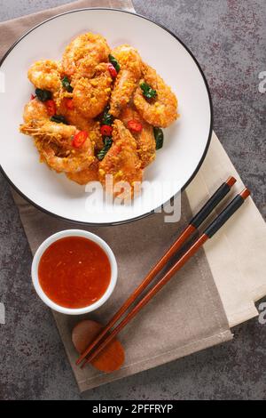 Fried shrimp with salted egg yolks, curry leaves and chili pepper close-up in a plate on the table. Vertical top view from above Stock Photo