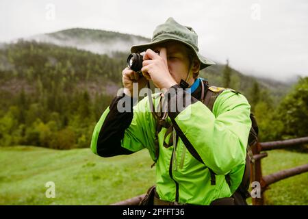 Young man tourist with backpack taking photos during hiking in mountains Stock Photo