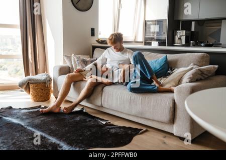 Young cheerful multinational couple hugging while resting on sofa at home Stock Photo