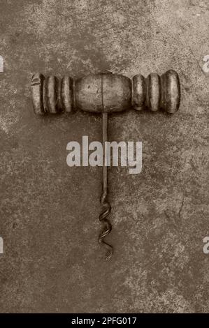 Sepia image of vintage corkscrew with wooden handle lying on tarnished metal Stock Photo