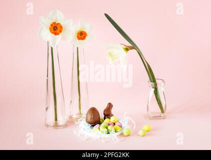 Easter still life with three daffodils in glass vases, easter eggs and mini chocolate bunny Stock Photo