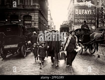 French Immigration - 'Here is a train coming from the north, we see several families who, terrified by the raid of the Germans, come to ask for hospitality'. Family with luggage (men, women and children) walking up a street with their luggage in the middle of road traffic. Horse-drawn carriages, coachman. Immigration. First World War. Paris. Great War. War of 14-18. North Station? Stock Photo