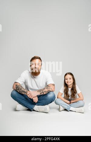 Positive tattooed father and preteen kid looking at camera while sitting on grey background,stock image Stock Photo