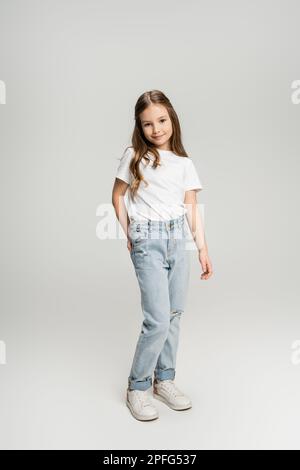 Full length of preteen girl in jeans and t-shirt posing and smiling on grey background,stock image Stock Photo