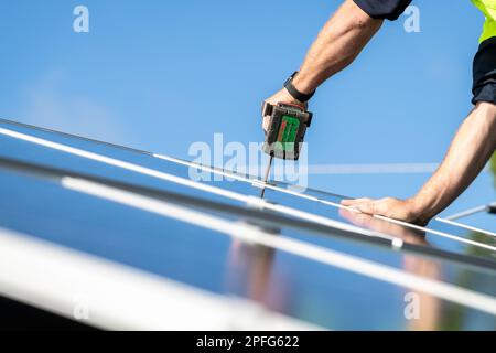Unidentified electrician installing solar panels on the house roof using cordless screwdriver Stock Photo