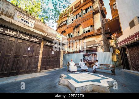 Portrait of Saudi men sitting on benches and relaxing in front of old coral townhouse at the historic district Al-Balad in Jeddah, KSA, Saudi Arabia Stock Photo