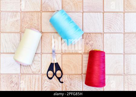 Multi colored threads and tailor scissors on a wooden plaid surface Stock Photo