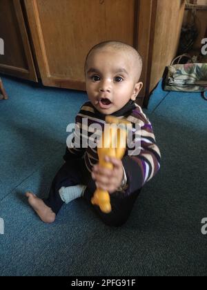 Asian cute baby sitting and playing a small toy on soft mat at home. The kid holding the toy and question about how to play it. Stock Photo