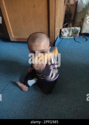 Asian cute baby sitting and playing a small toy on soft mat at home. The kid holding the toy and question about how to play it. Stock Photo