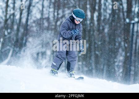 Little skier riding downhill with snow splash. Child skiing in mountains. Active teenage boy with safety helmet, goggles and ski poles running down Stock Photo